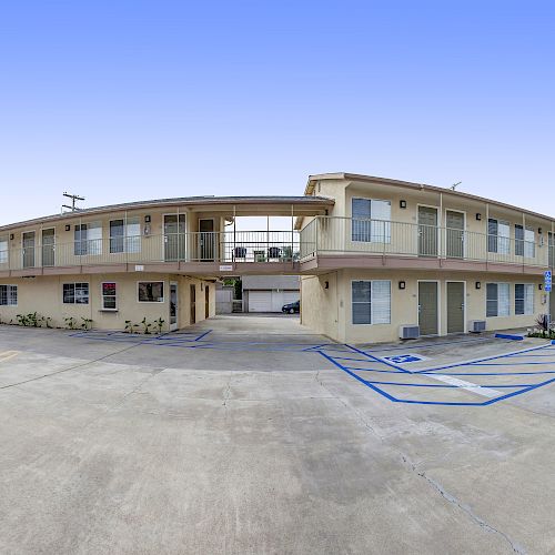 The image shows the exterior of a two-story motel building with parking spaces, including accessible spots. A sign reading 