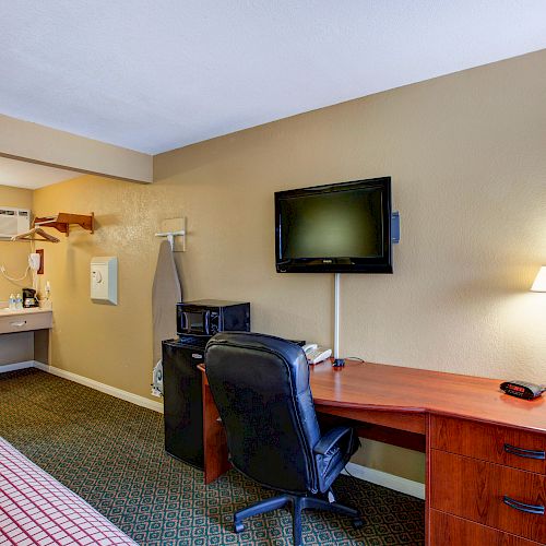 A hotel room with a bed, desk, TV, lamp, microwave, and sink area, featuring a cozy and functional setup.