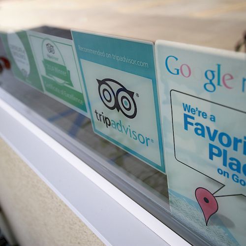 The image shows signs on a window for TripAdvisor and Google Maps, indicating the place is a favorite on these platforms.